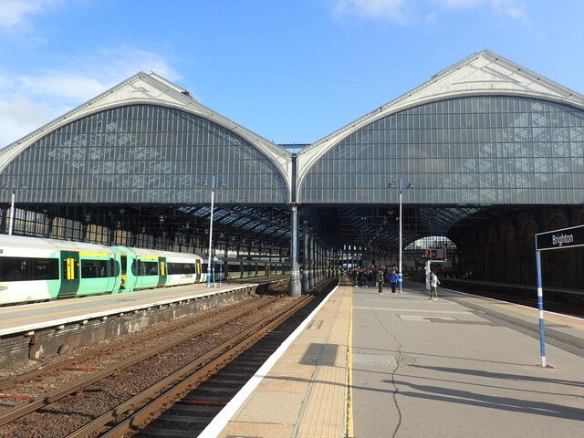 Brighton station platform beneath its curved glass roof, with a Brighton station sign. Photo by Marathon, CC BY-SA 2.0, taken 2023.